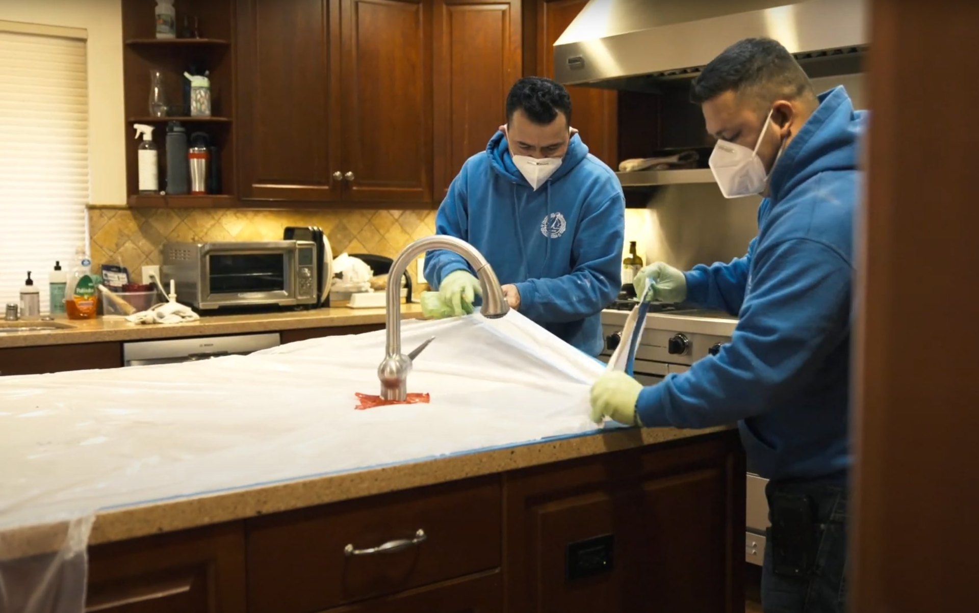 Professional water damage restoration technicians working in kitchen with protective equipment and specialized tools